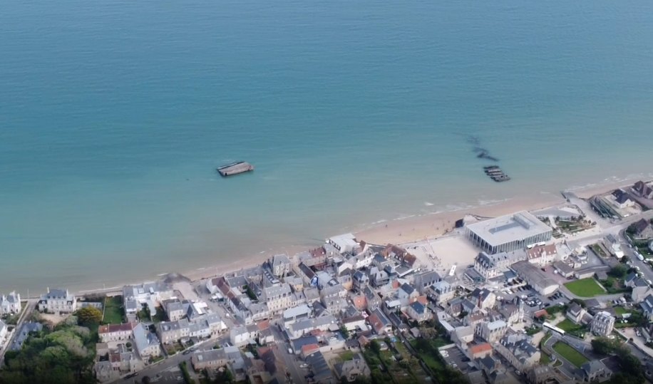 Aerial view of Arromanches-les-Bains with visual markers for the Cale Neptune boarding area and the D-Day Museum.
