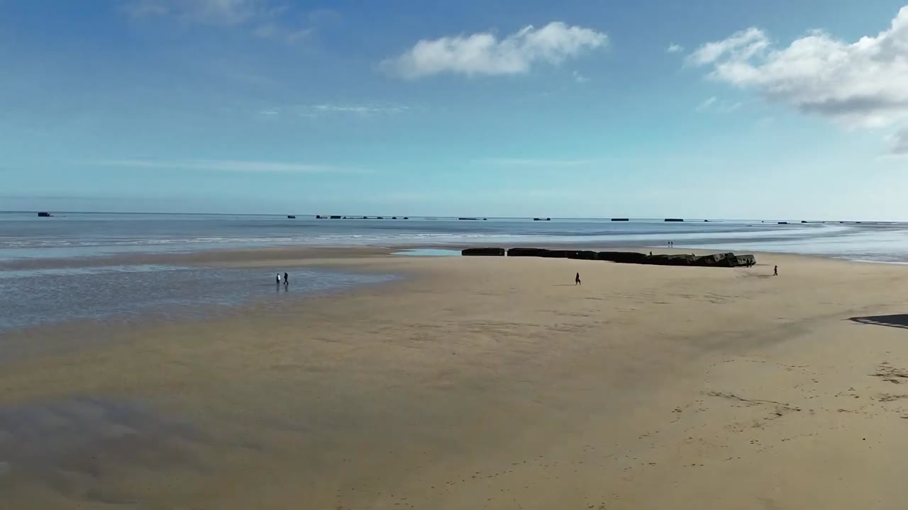 Aerial view over the beach of Arromanches-les-Bains at low tide, with the Phoenix caissons of the Mulberry harbour offshore.