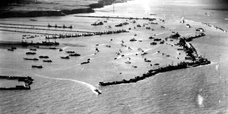 Historic aerial view of the Mulberry artificial harbour in operation at Arromanches: caissons, piers and Allied ships unloading.